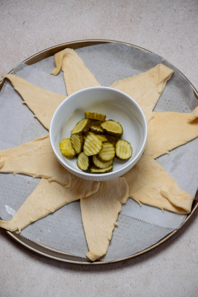 add a layer of parchment paper to your pizza pan, and place a serving bowl in the center. Arrange the first package of crescent rolls around the center, with the thickest portion lined up with the bowl edge.