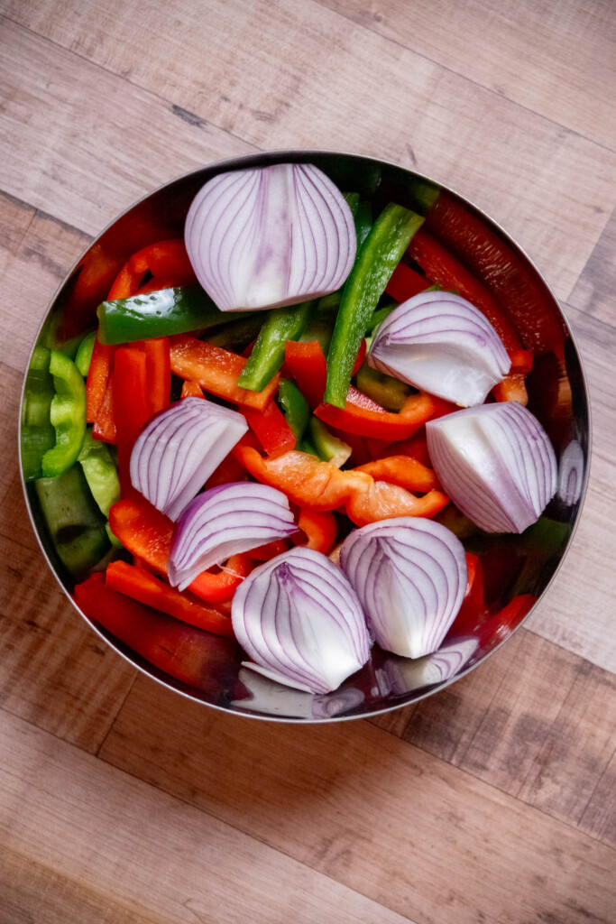 remove the core, ribs, seeds, and stem from the bell peppers, and slice into &frac12;" thick slices. Cut  onions into quarters, and add to a mixing bowl