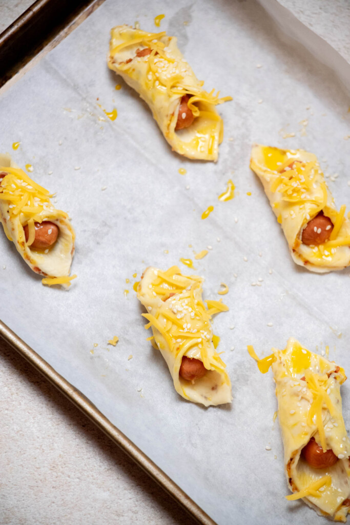 while they chill, preheat the oven. Once chilled, brush with egg wash to coat, then sprinkle on sesame seeds and reserved 2 tablespoon of shredded cheddar. 