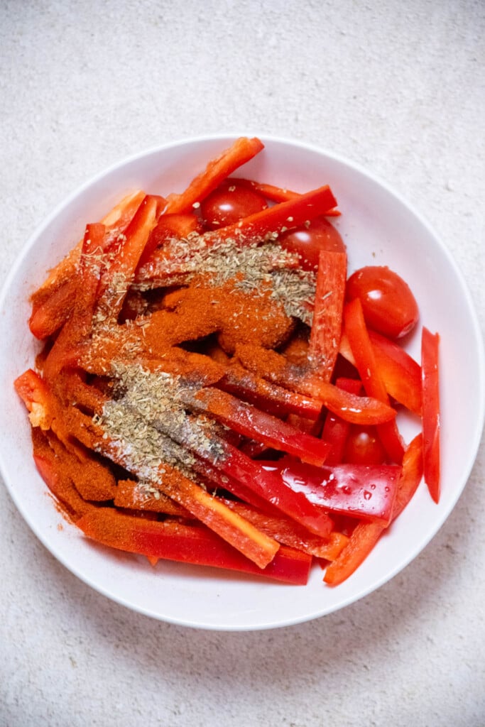 slice your bell pepper into thin strips, and add to a bowl with the grape tomatoes, olive oil, and spice blend. 