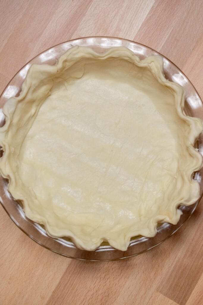 Use the trimmed puff pastry pieces to fill and gaps around the edge, and press to combine with the dough in the pie plate. Crimp the edges, then place the whole dish in the fridge or freezer to chill. 
