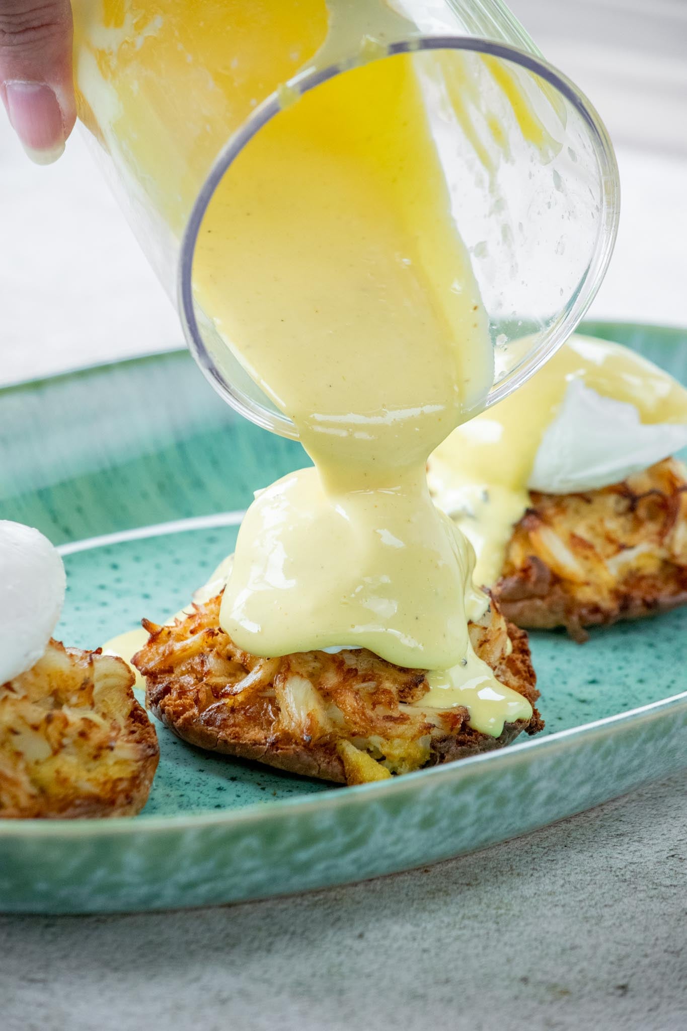 Pouring the Old Bay hollandaise over the top of each poached egg on a muffin.