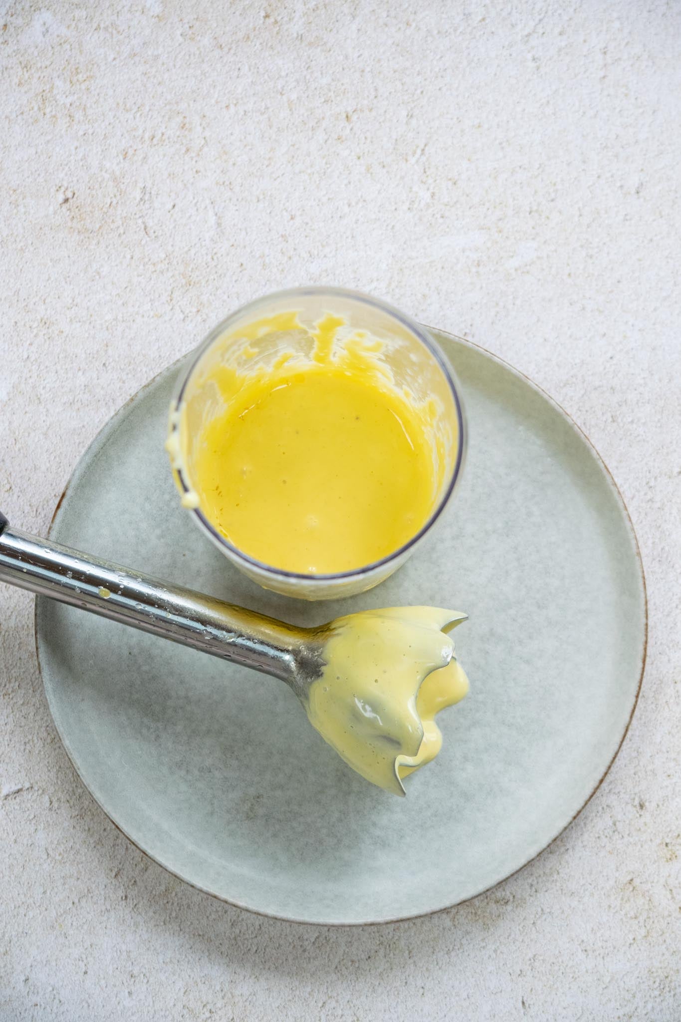 Blended hollandaise in a cup with the immersion blender resting to the side.