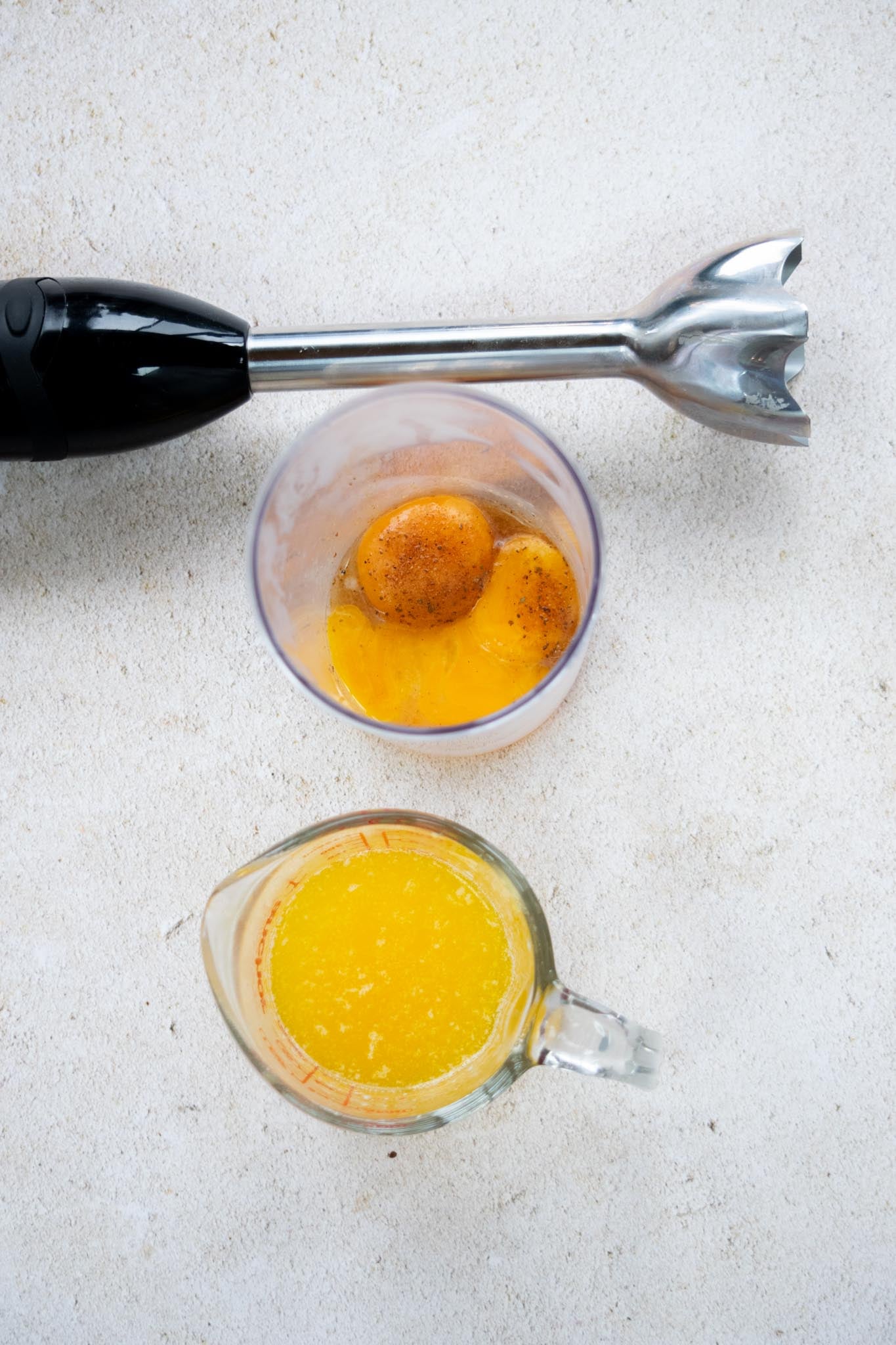 Egg yolks and ingredients in a tall cup with melted butter on the side.