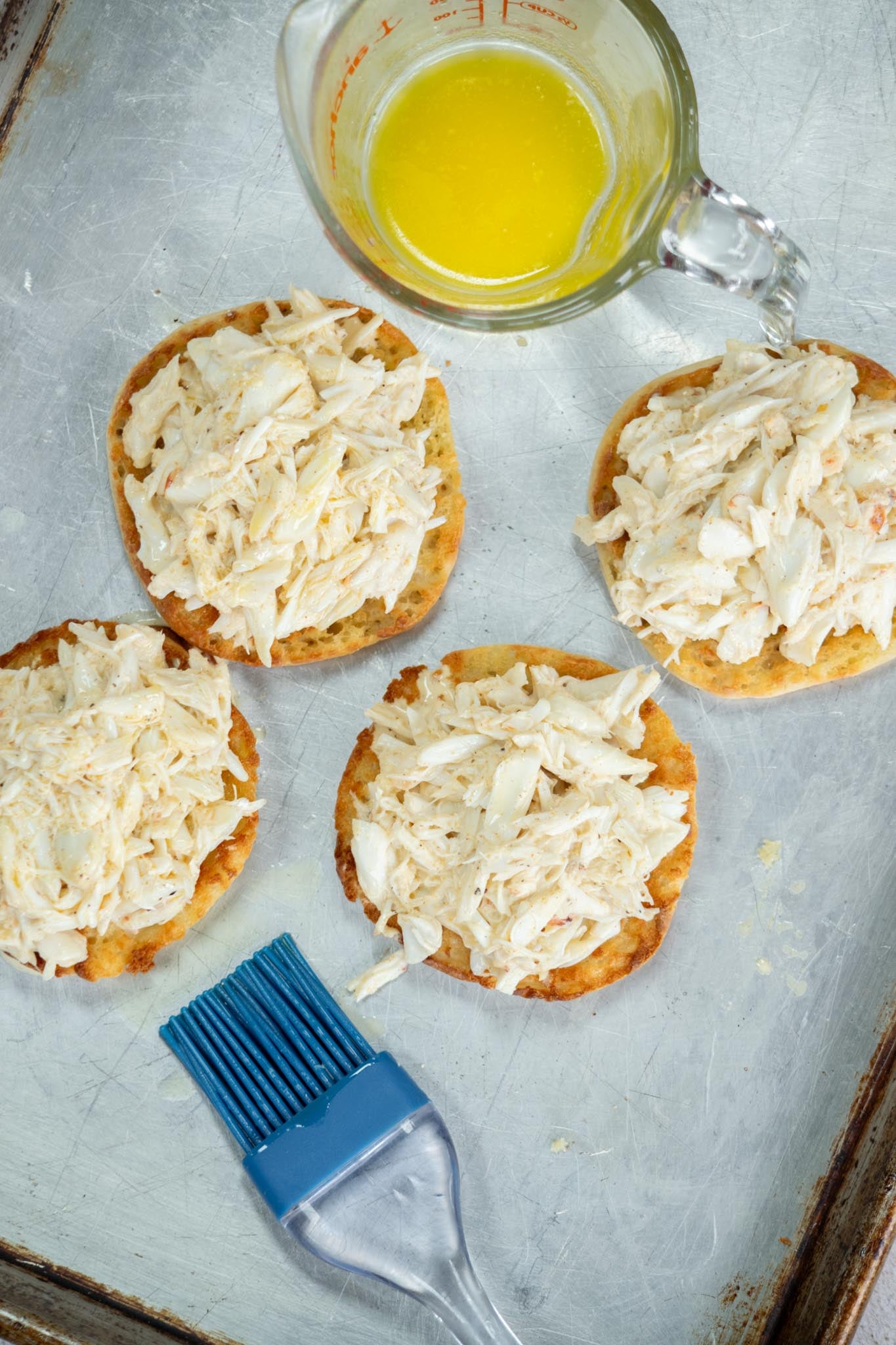 Crab mixture added to each English muffin with butter and a pastry brush on the side.