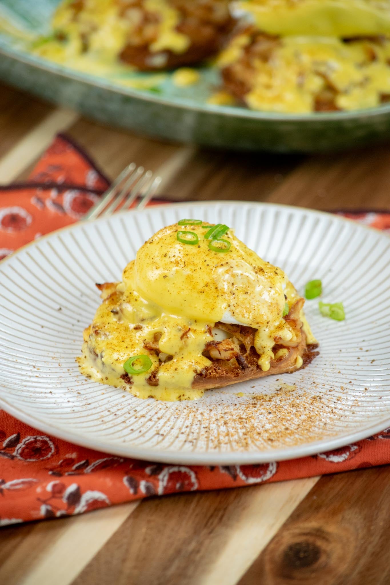 Crab Benedict on a white plate sprinkled with green onions.