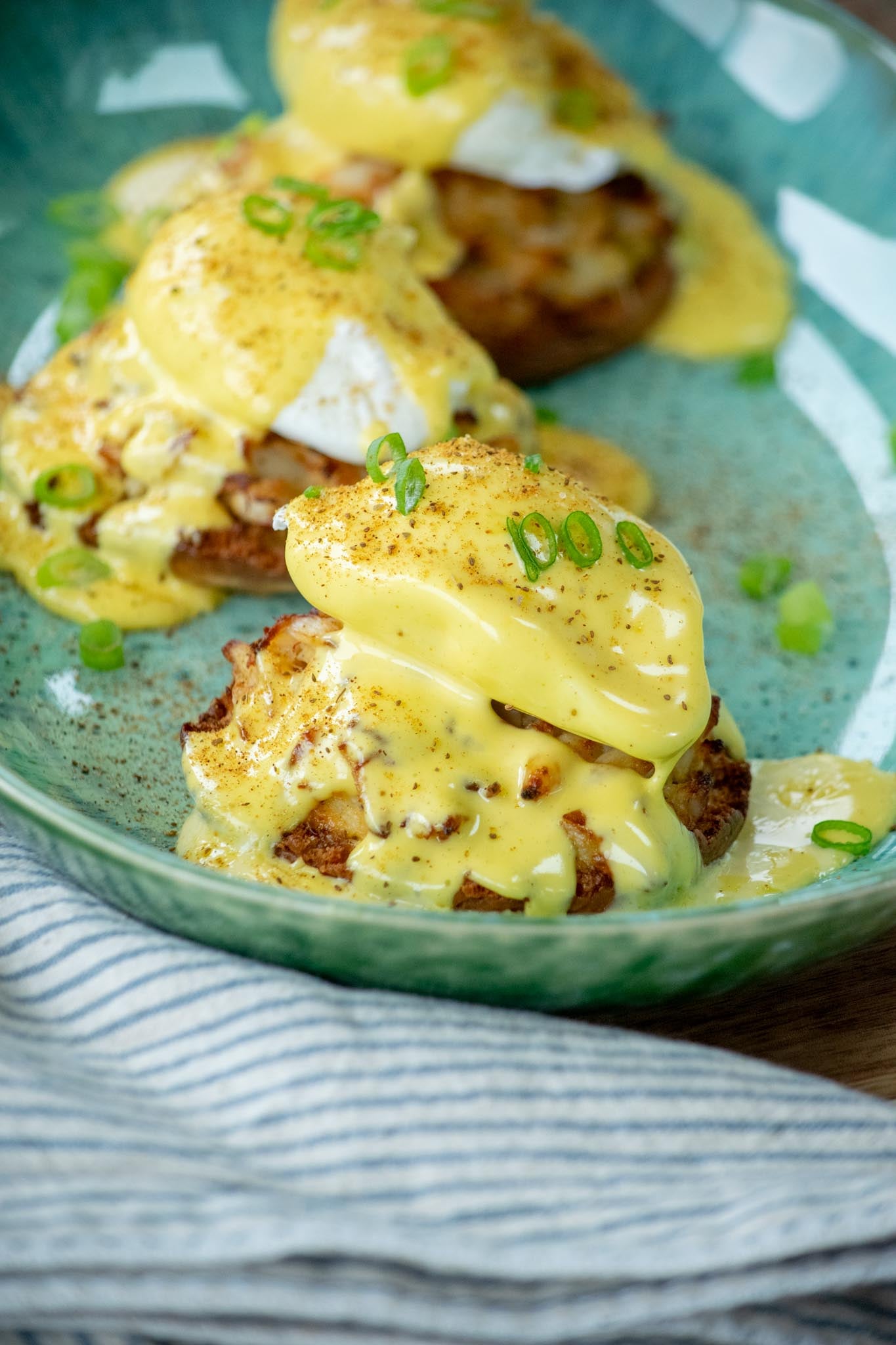 Crab benedicts on a blue plate garnished with Old Bay and green onions.