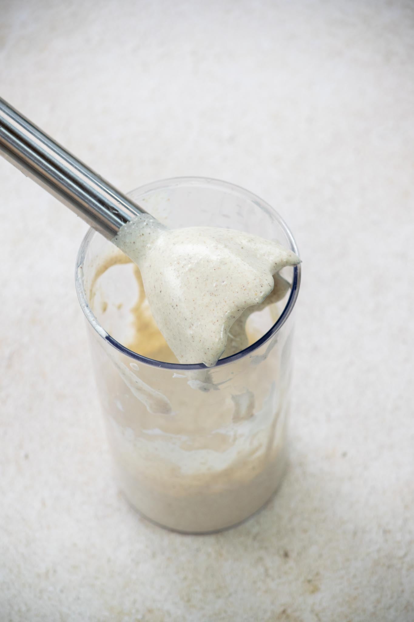 The immersion blender held over the glass of blended dressing.