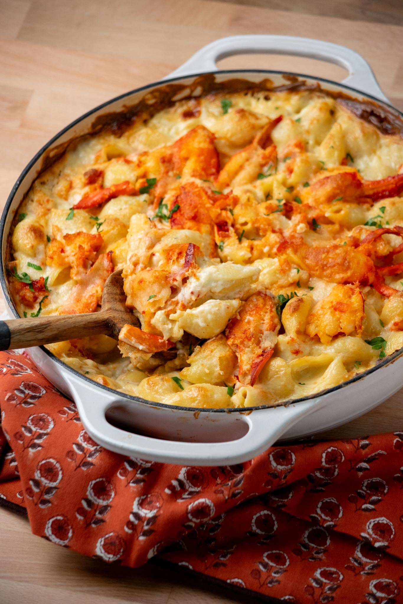 A pot of lobster macaroni and cheese with a wooden spoon lifting up a serving.