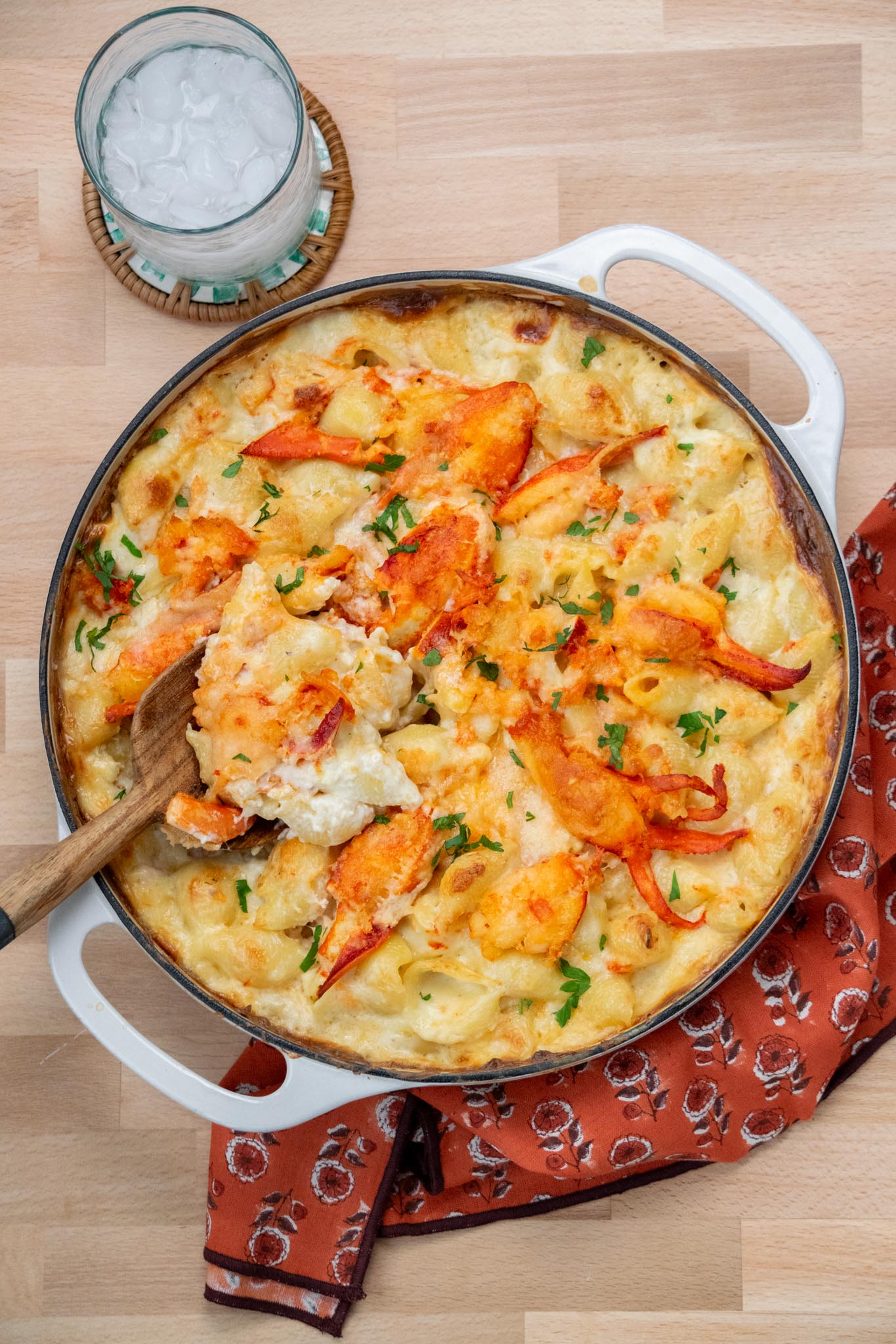 A casserole dish of macaroni and cheese lobster recipe with a glass of water on the side.
