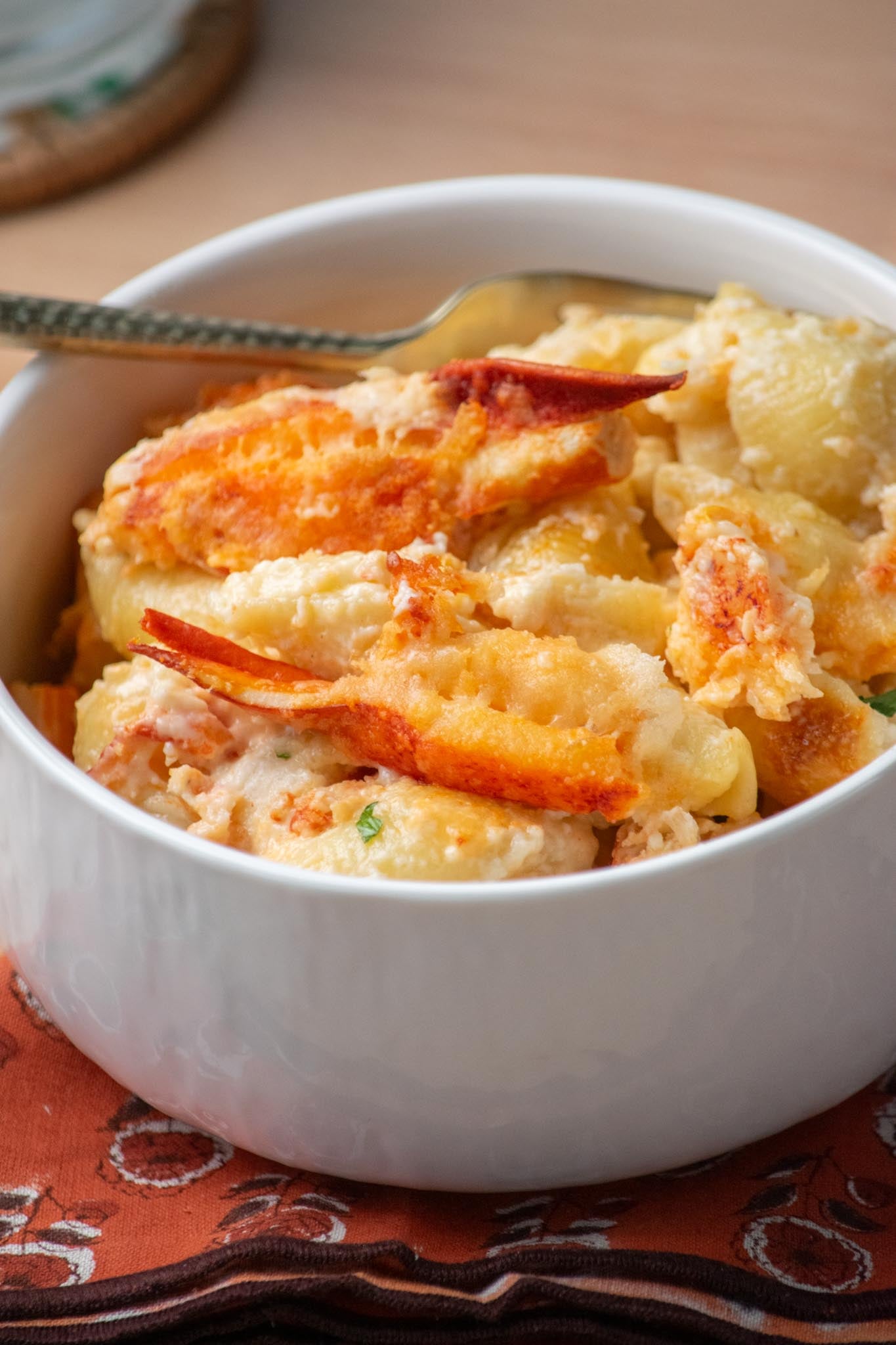 A bowl of lobster mac and cheese with brie on the table and a fork resting on the side.