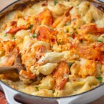 A round casserole dish of baked lobster mac and cheese with a wooden spoon resting in the dish.
