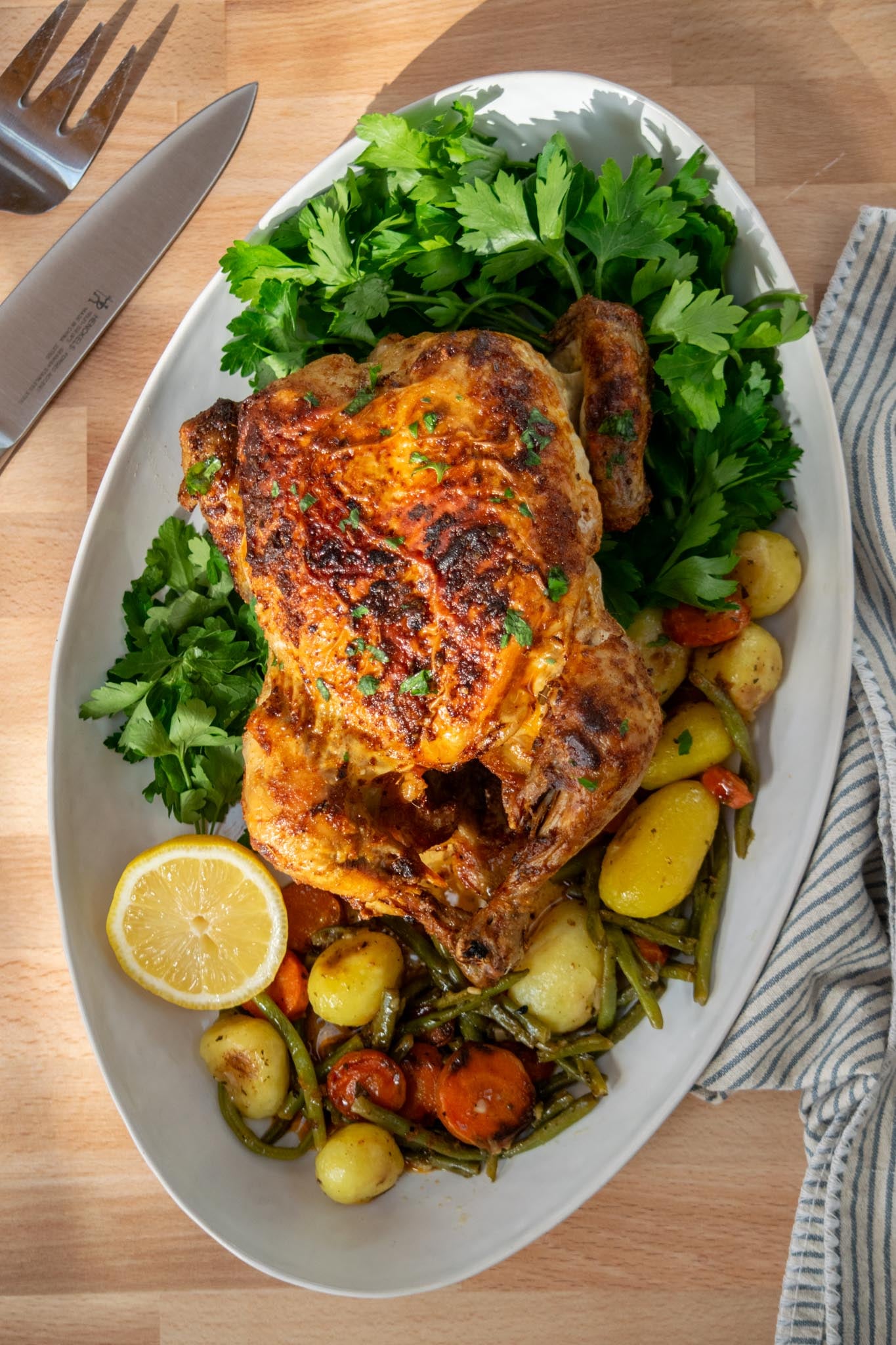 Air fryer rotisserie chicken on a platter with vegetables, potatoes, and parsley.