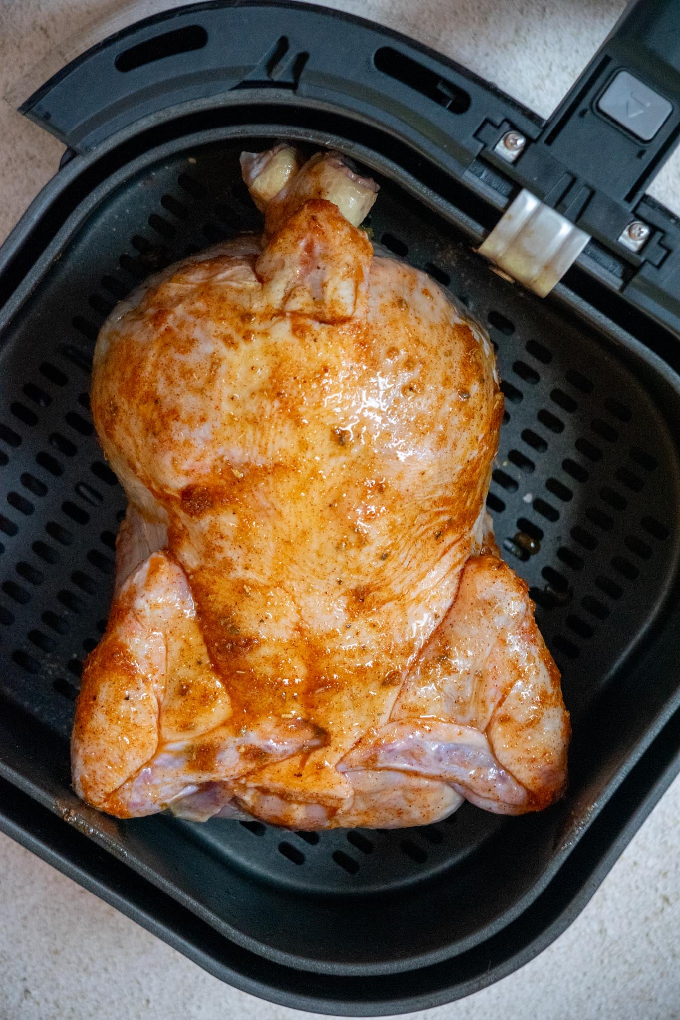 Seasoned chicken placed in the air fryer basket breast side down.