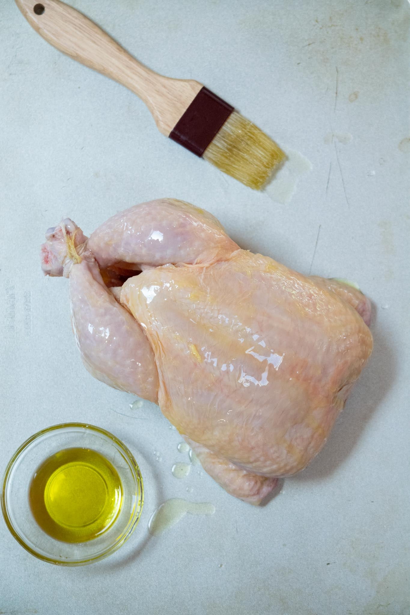 Whole chicken brushed with olive oil and the pastry brush and dish of oil to the side.