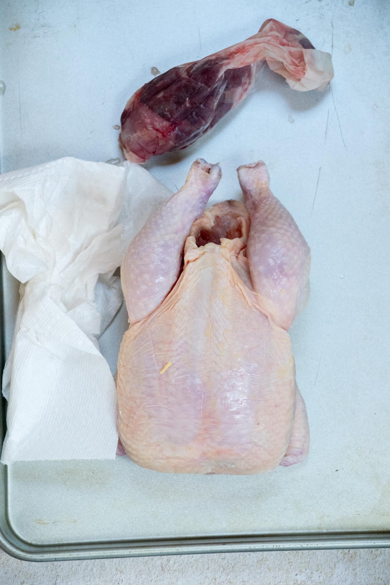 Whole chicken on a cutting board with a paper towel and bag of giblets to the side.