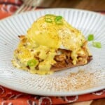 Crab Benedict on a plate with hollandaise and green onions.