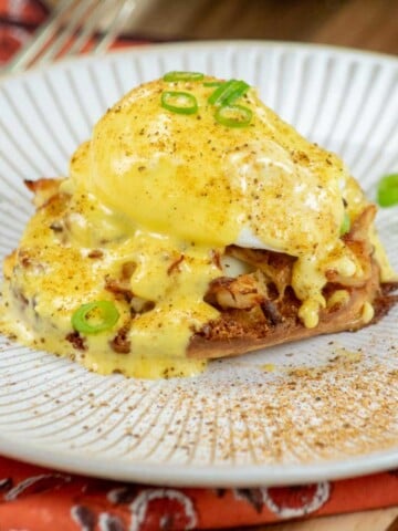 Crab Benedict on a plate with hollandaise and green onions.