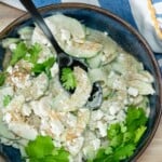 A bowl of cucumber feta salad with the spoon resting in the bowl.