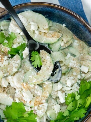 A bowl of cucumber feta salad with the spoon resting in the bowl.