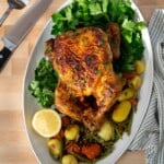 Air fryer roasted chicken on an oval platter with vegetables and herbs.