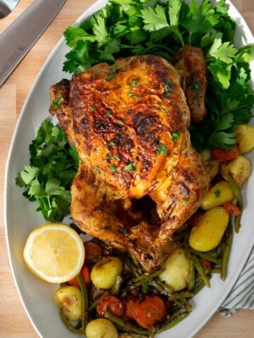 Air fryer roasted chicken on an oval platter with vegetables and herbs.